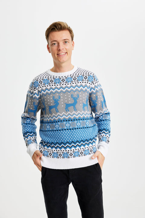En smilende mand med hænderne i lommen iført en blå julesweater.