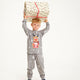 Et barn med en gave over hovedet er iført en grå julepyjamas.
