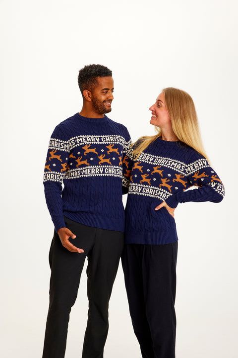 En mand og en dame kigger på hinanden og er begge iført en blå julesweater med rensdyr på.