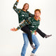 En kvinde der sidder på ryggen af en mand, hvor de begge er iført samme grønne julesweater.